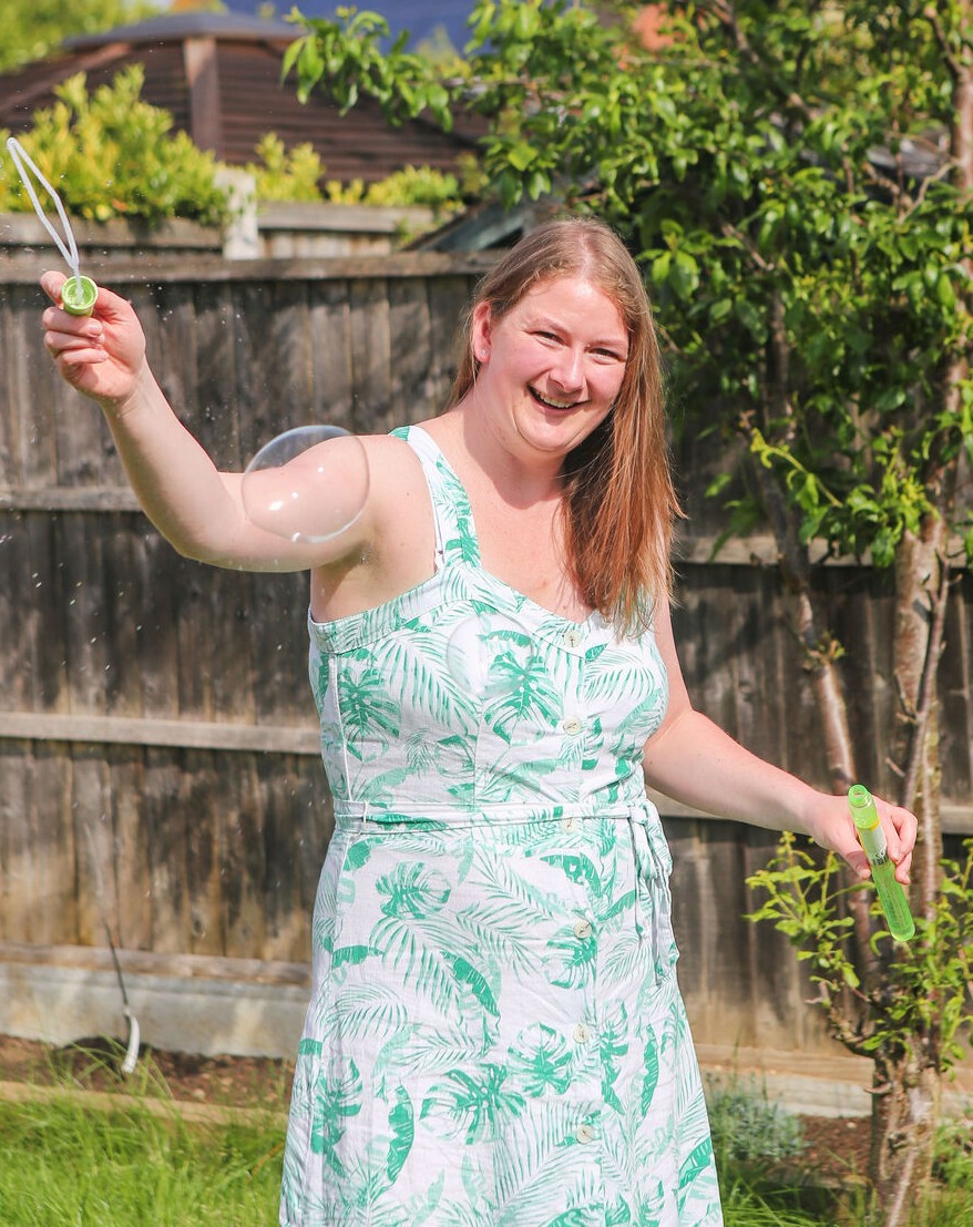 Woman in a green sundress blowing bubbles in a garden.