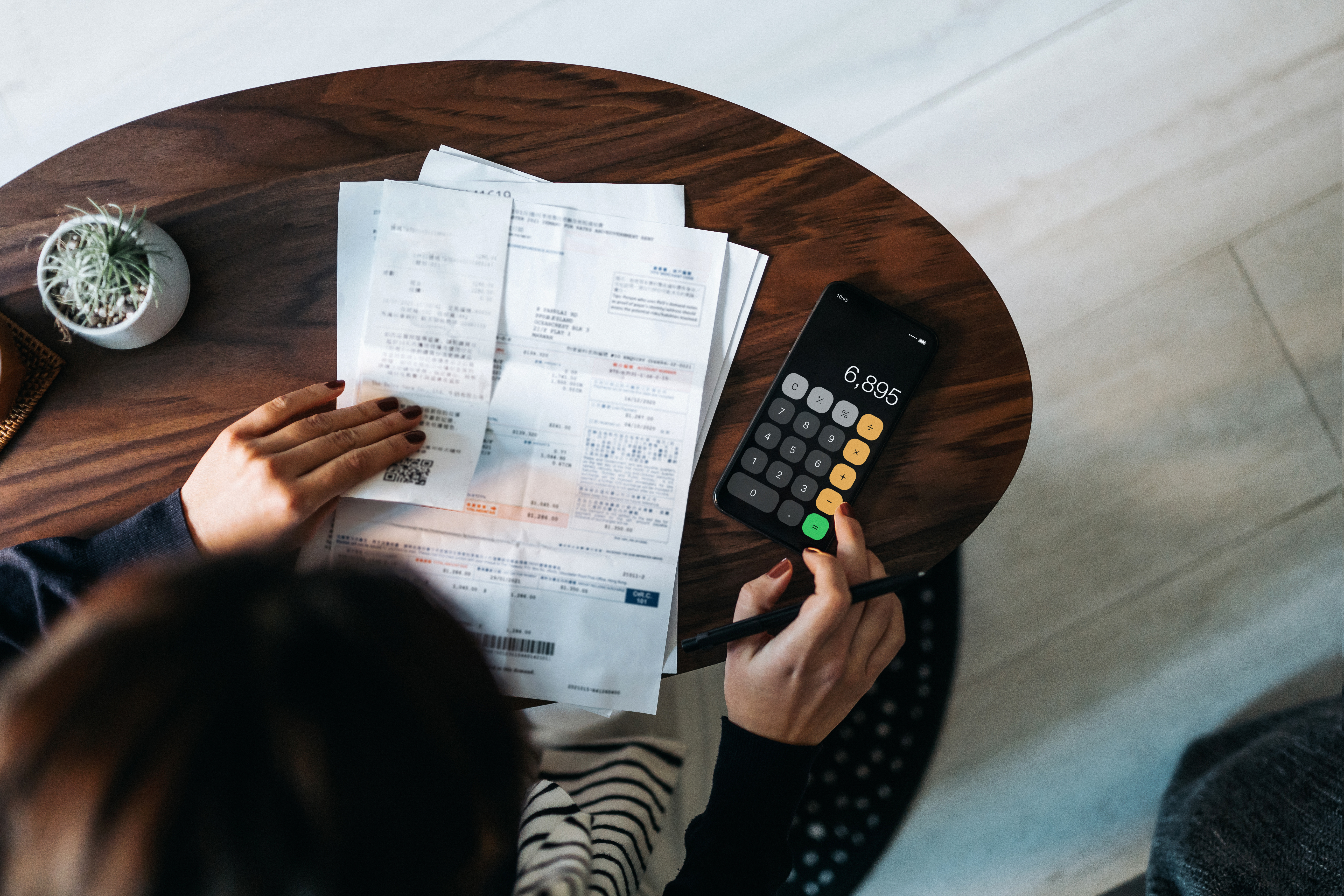 Woman reviewing bills and using a calculator app on her phone.