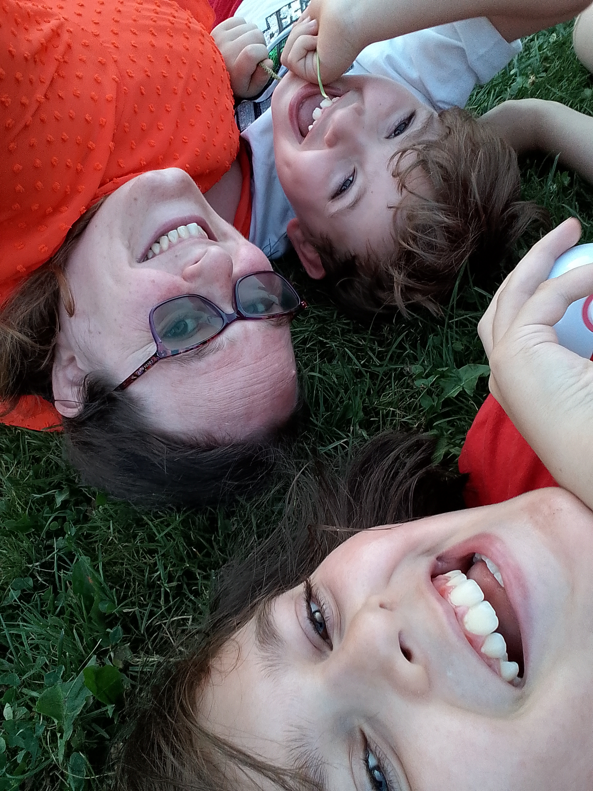 A woman and two children lying on the grass, smiling.